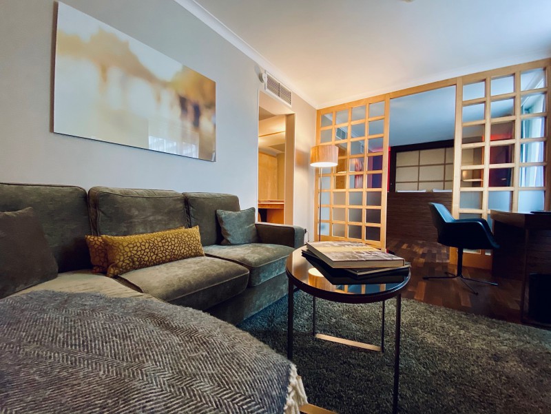 Die Suite im Hotel Palace Berlin kombiniert Wohn-, Arbeits- und Schlafbereich in einem stilvollen Ambiente. Mit Sofa, Schreibtisch, Fernseher und dekorativen Pflanzen bietet sie Komfort, während warmes Licht und Holzboden für Gemütlichkeit sorgen.