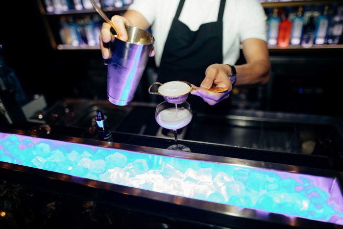 Ein Cocktail wird im House of Gin im Hotel Palace Berlin zubereitet. Ein Barkeeper gießt die Zutaten ein, während das Glas stilvoll angerichtet wird.