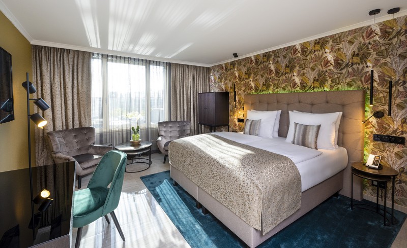 Business premium in Hotel Palace Berlin room with large bed, floral wallpaper, armchair, gray sofa, and daylight through sheer curtains.