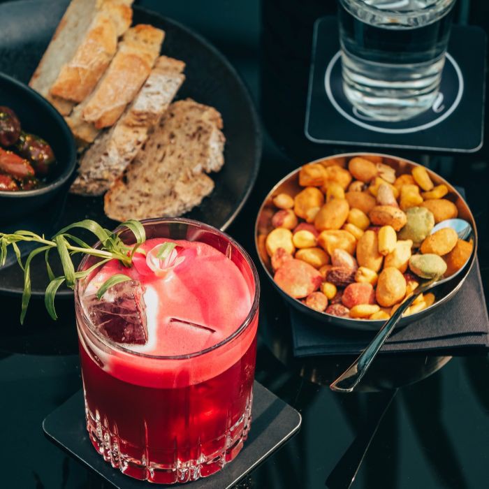 Roter Cocktail, ein Glas Wasser und Fingerfood im House of Gin im Hotel Palace Berlin. 