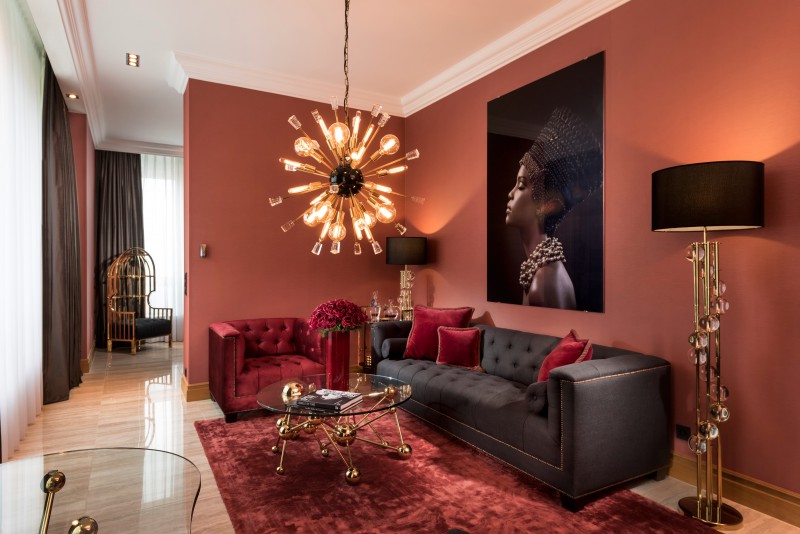 Elegant hotel Corner Suite  living room in Hotel Palace Berlin in central Berlin with modern chandelier, velvet sofas, glass coffee table, and a large portrait on the wall, featuring floor lamps and refined glass accents.