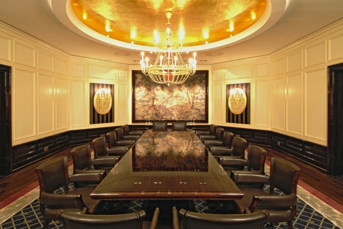 Luxuriöser Konferenzraum Gobelinzimmer mit langem Holztisch, umgeben von Lederstühlen. Ein großer Kronleuchter hängt von der goldenen Decke, während elegante Wandpaneele und ein großes Gemälde dem Raum Raffinesse verleihen.