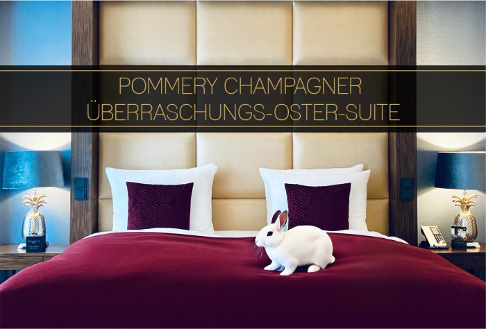 Photo of the bed and headboard in a suite at Hotel Palace Berlin, featuring a white rabbit on the bed. The image promotes the Pommery Easter Suite with the text 'Pommery Champagne Surprise Suite.'