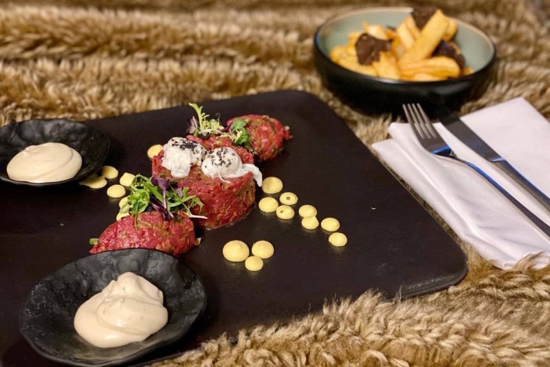 Room Service - Ein Rindfleisch Tartar, serviert auf einem auffälligen roten Teller, der unter einer transparenten Abdeckung präsentiert wird. Ein Highlight im Restaurant beef45 des Hotel Palace Berlin.
