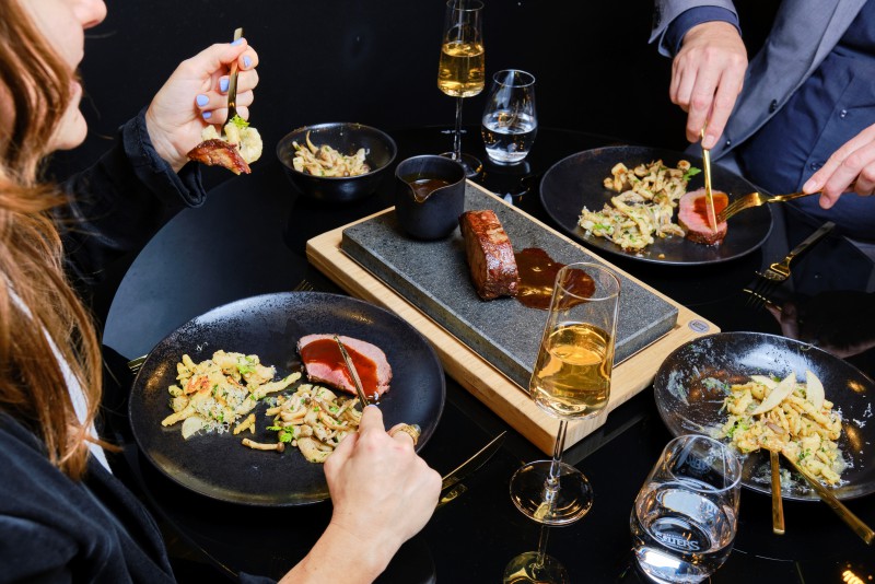 A man and woman enjoy an elegant dinner at beef45 restaurant in Hotel Palace Berlin. The table is set with steak, pasta, and wine glasses, surrounded by a luxurious atmosphere in central Berlin.