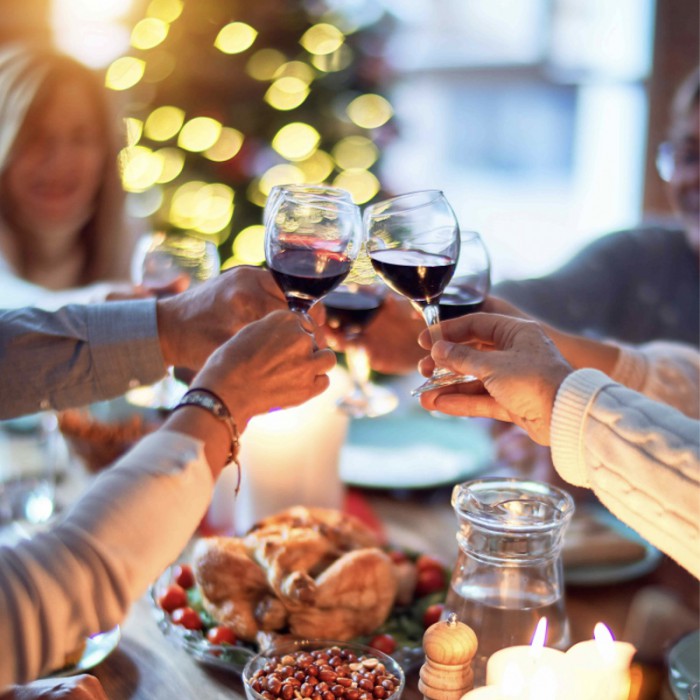 Menschen stoßen mit Rotweingläsern an einer festlich gedeckten Weihnachtstafel voller köstlicher Speisen an und genießen die festliche Atmosphäre.