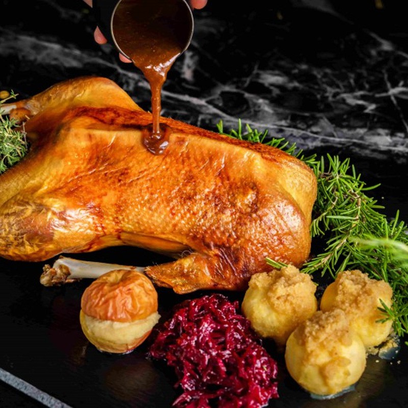 Martins- und Weihnachtsgans to Go - Knusprig gebratene Gans mit Apfel, Rot- und Weißkohl aus dem 'Goose to Go'-Weihnachtsangebot im Hotel Palace Berlin, festlich angerichtet.