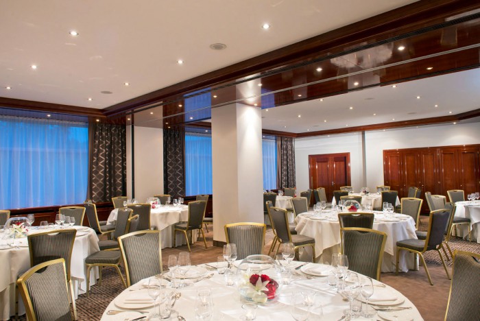 Der Bankettsaal im Hotel Palace Berlin mit runden, weiß gedeckten Tischen, eleganten Gläsern und floralen Mittelstücken. Große Spiegel, Holzvertäfelung und sanfte Beleuchtung schaffen eine stilvolle Atmosphäre für Veranstaltungen.